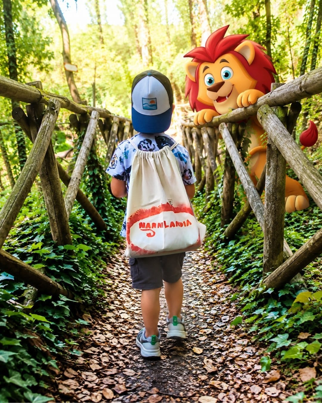Scoprire giocando a Narnilandia Un bambino con lo zainetto di Narnilandia cammina su un sentiero nel bosco a Narni; il leone di Narnilandia lo aspetta appoggiato alla staccionata