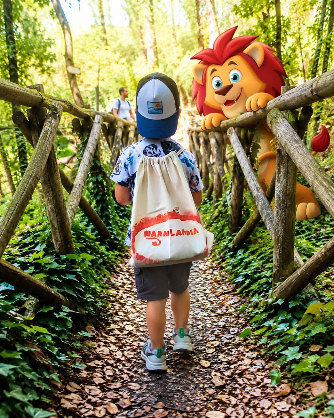 Scoprire giocando a Narnilandia Un bambino con lo zainetto di Narnilandia cammina su un sentiero nel bosco a Narni; il leone di Narnilandia lo aspetta appoggiato alla staccionata