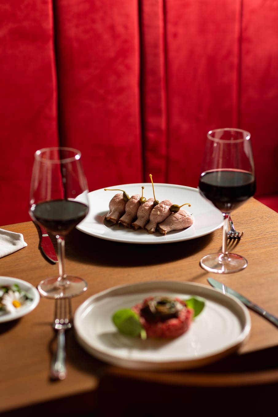 Piatti serviti al tavolo con calici di vino rosso nella sala di Catarina Bistrot, ristorante nel centro di Torino