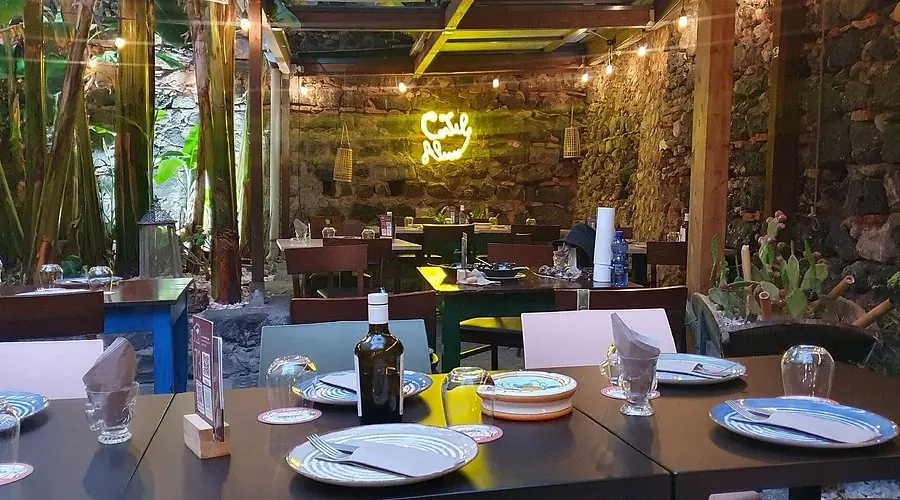 Il cortile interno di Al Cortile Alessi a Catania, con tavoli apparecchiati tra piante e muri in pietra lavica