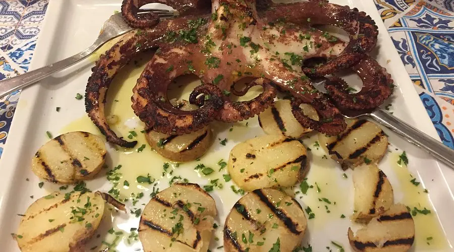 Polpo alla griglia con patate e prezzemolo, piatto tradizionale mediterraneo ricco di sapore.