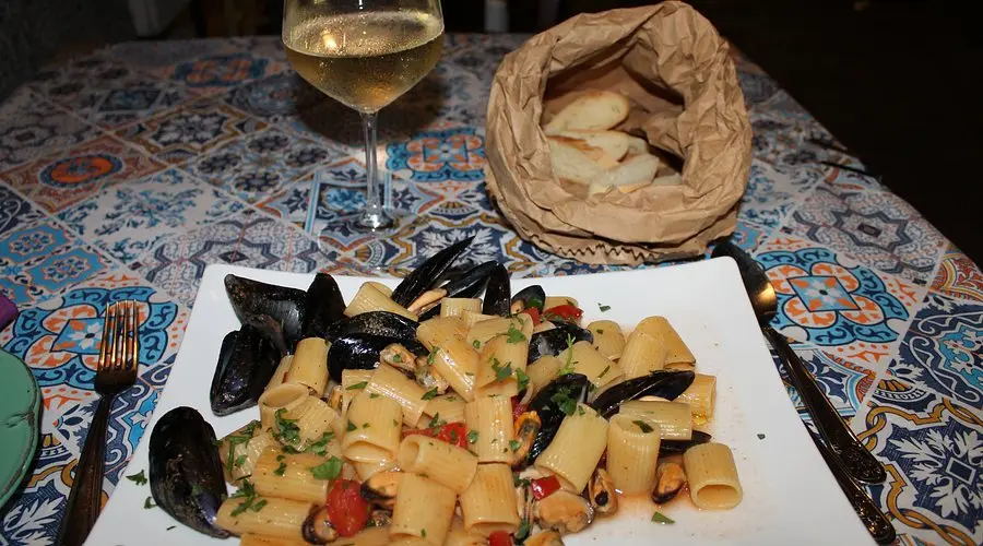 Delizioso piatto di pasta con le cozze fresche, servito con un sugo aromatico a base di aglio, olio d'oliva, pomodorini freschi e prezzemolo tritato. Un piatto di mare dal sapore intenso e mediterraneo, perfetto per gli amanti della cucina Catanese.