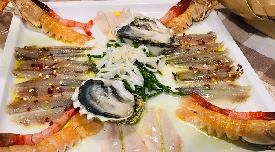 Delizioso piatto di pesce crudo fresco, con alici, salmone e gamberi  ostriche su un letto di ghiaccio tritato, decorato con fettine di lime, . Un'opzione gourmet per gli amanti della cucina Siciliana a-casa-di-pino