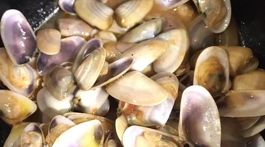 Piattino di telline fresche appena sgusciate, servite con un filo di olio d'oliva extravergine, aglio, prezzemolo e un tocco di pepe nero. Un piatto di mare delicato e saporito, perfetto per gli amanti dei frutti di mare freschi.