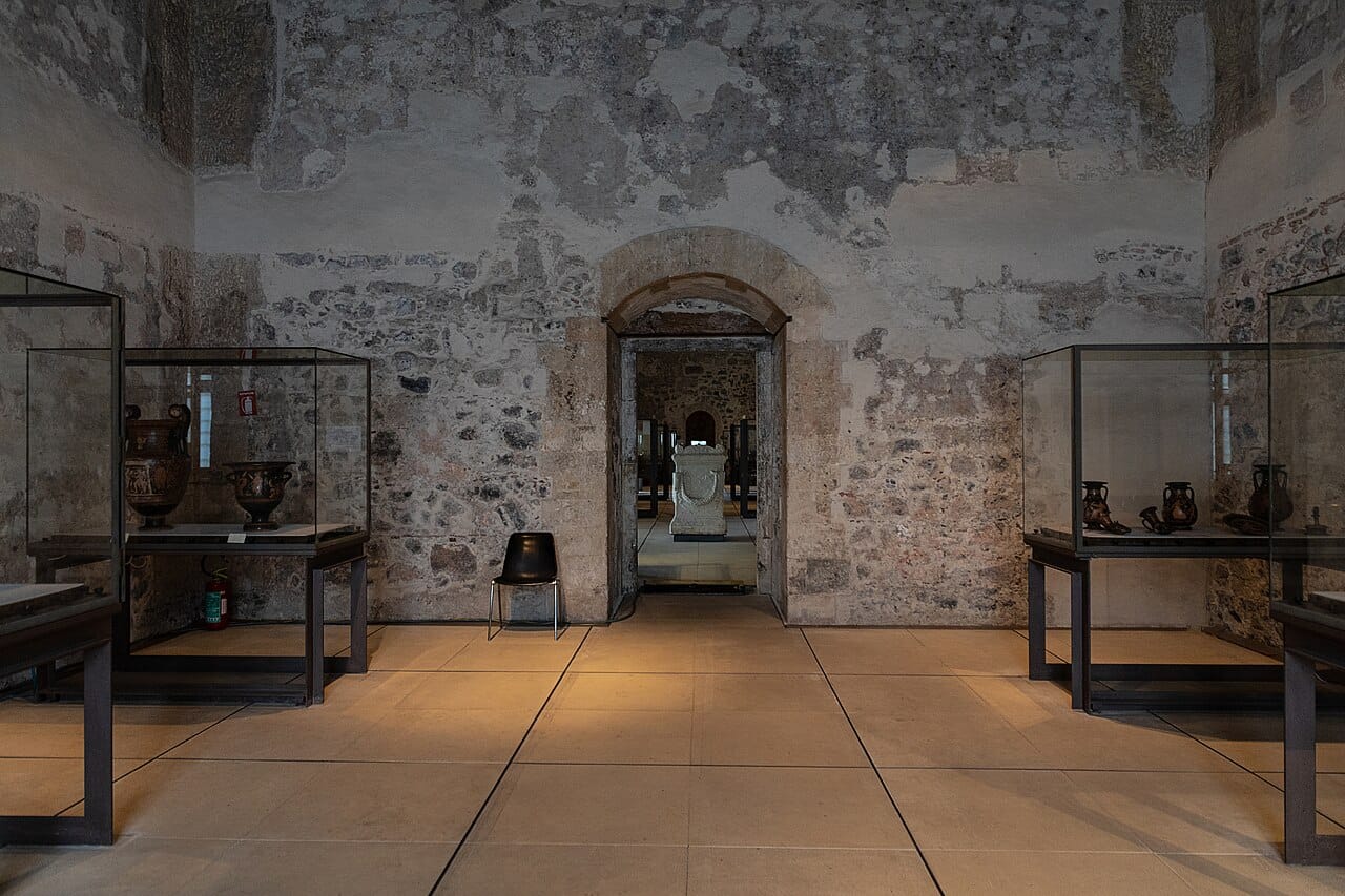 Una sala del Museo Civico al Castello Ursino di Catania con vetrine di vasi greci e un sarcofago di marmo