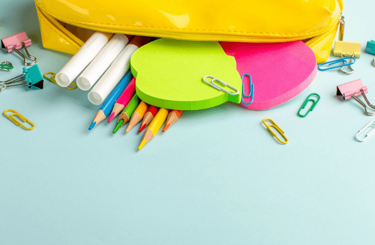 Astuccio giallo su piano azzurro con matite colorate, graffette, adesivi, pennarelli colorati, post it, mela verde, rosa, vista dall'alto, come si dice astuccio in inglese