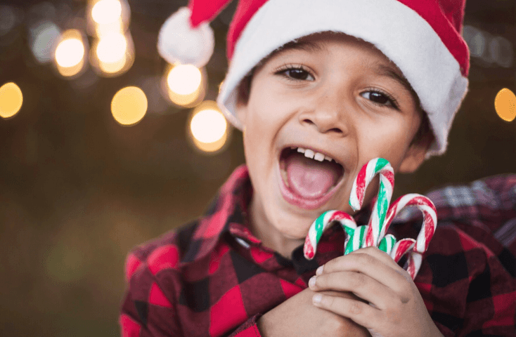Bambino felice e sorridente; cappellino rosso e pompom di Natale; bastoncini di zucchero colorati, bianco, rosso, verde; vista frontale; Poesie di Natale in inglese tradotte in italiano