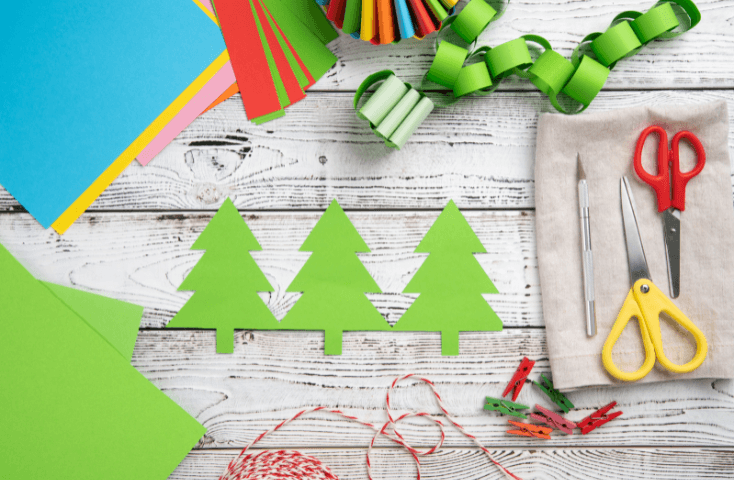 Albero di natale di carta verde, cartoncini colorati verde, azzurro, arancione, giallo; filo colorato rosso e bianco, forbici mollette, ghirlanda di carta; vista dalll'alto;