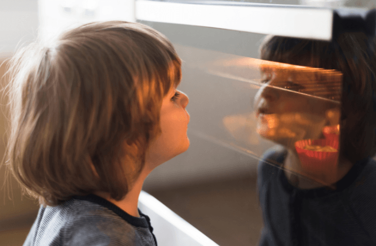 Bambino curioso guarda leccarda nel forno con puncake in cottura, bimbo attento, vista frrontale, quattro ricette dolci da preparare con i bambini