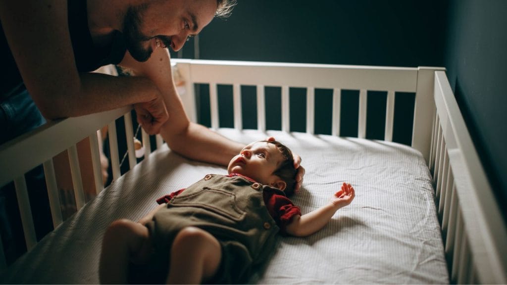 Papà chinato sul lettino che fa addormentare il suo bimbo neonato, ninne nanne in inglese