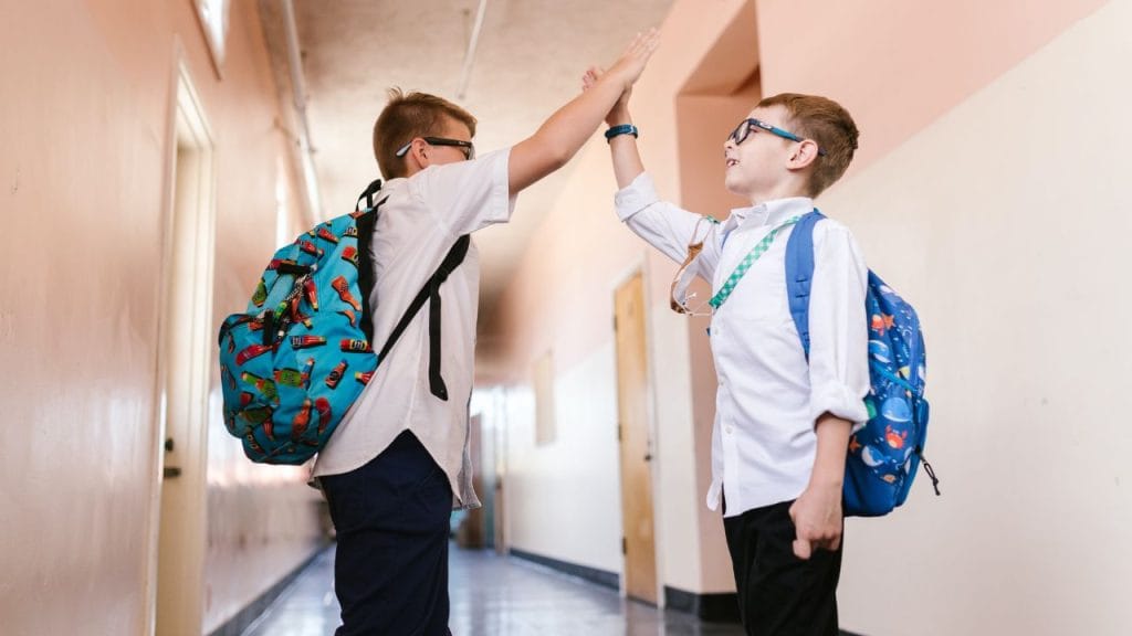Ragazzini che s battono il cinque alto nel corridoio della scuola con in spalla lo zaino, come si dice zaino in inglese