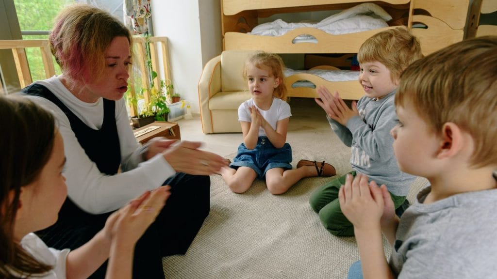 Mamma seduta a terra con bambini in cerchio che battono le mani, canzoncine in inglese per imparare le parti del corpo