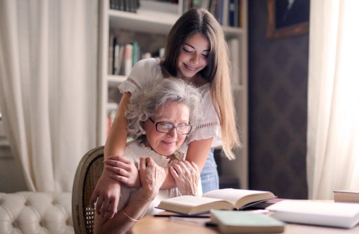 Nipote che abbraccia la nonna seduta al tavolo intenta a leggere un libro, come si dice nonna in inglese