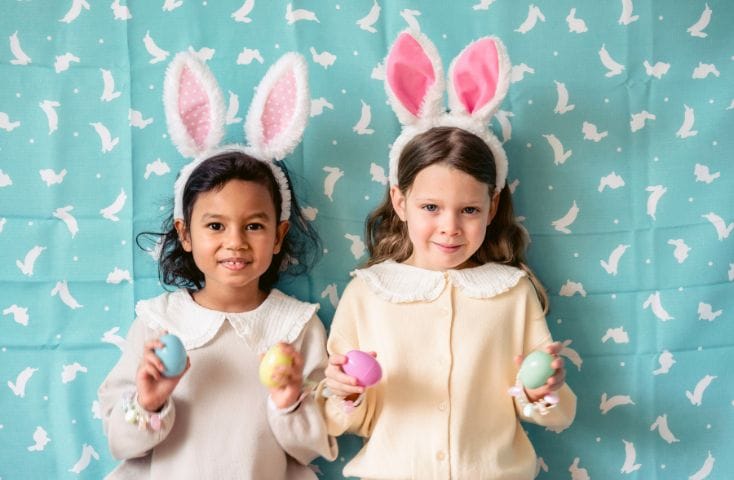 due bambine con le orecchie da coniglio che tengono in mano delle uova colorate, poesie e filestrocche pasquali in inglese per bambini