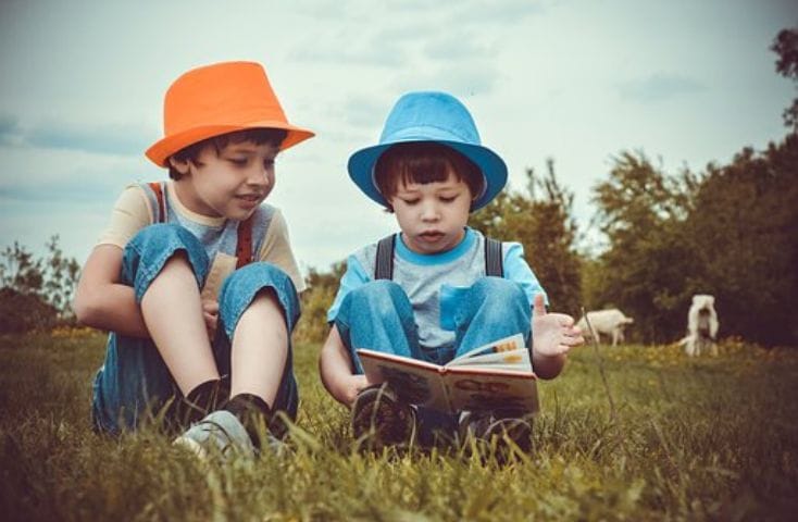 due bambini che leggono un libro in un prato indossando cappelli colorati, poesie e filestrocche pasquali in inglese per bambini