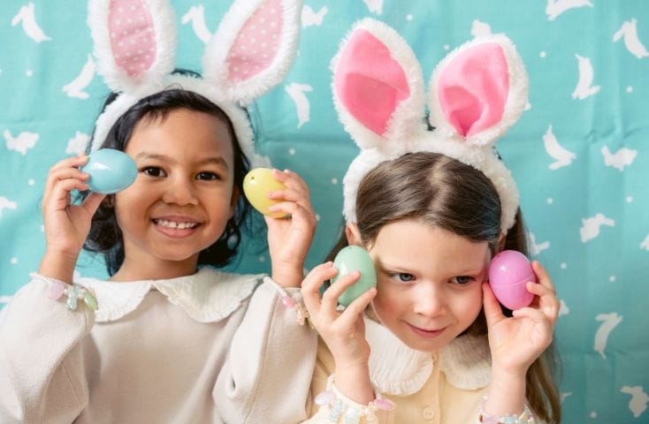 Due bambine con cerchietto con le orecchie del comiglio e due uova colorate in mano, come si dice Buona Pasqua in inglese