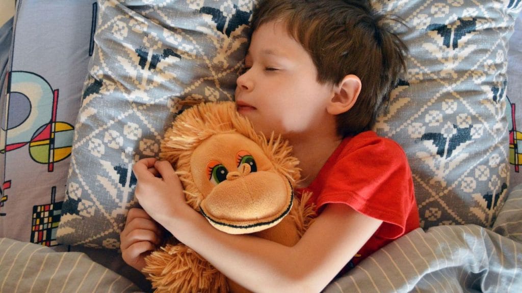 Bambino che dorme abbracciato a una scimmietta di peluche, 5 modi per dire a un bambino in inglese di andare a letto