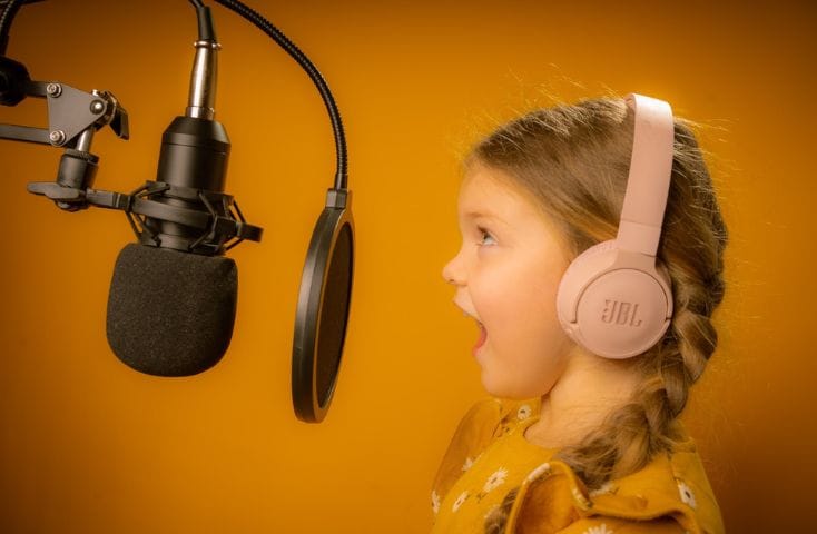 Bambina che canta al microfono con le cuffie, le 10 canzoncine più belle per bambini in inglese