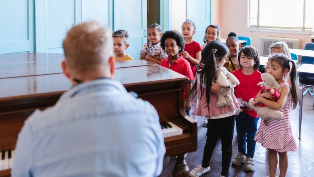 Gruppo di bambini che canta con insegnante al pianoforte, le 10 canzoncine più belle per bambini in inglese