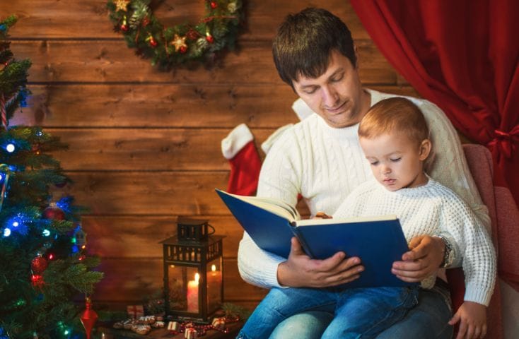 Papà che legge un libro col suo bimbo circondato dalle decorazioni natalizie