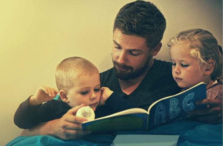 Papà che legge un libro al suo bimbo più piccolo e alla sua bimba più grandicella