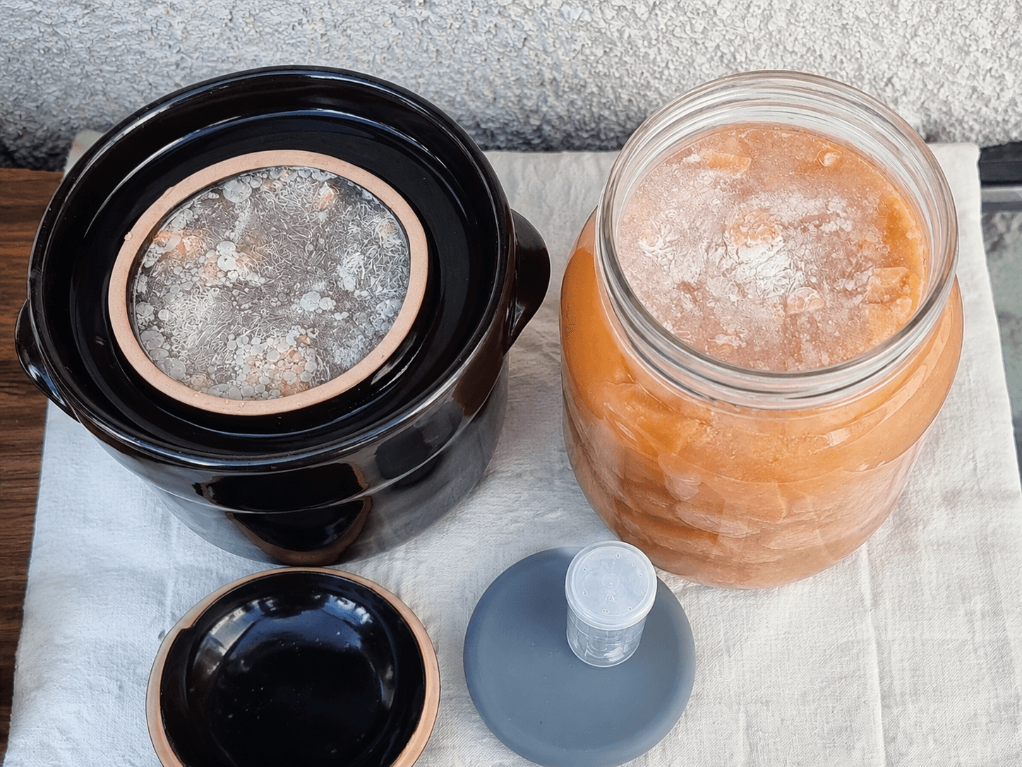 Crautiera in ceramica aperta a sinistra e vaso Kilner a destra, con carote in salamoia e formazione superficiale visibile
